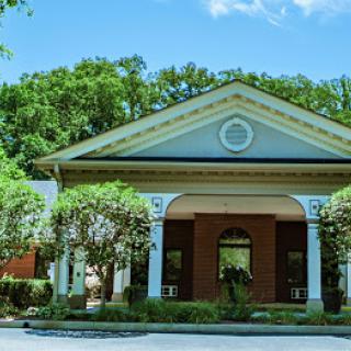 A beautiful architectural building with lush greenery surrounding its entrance on a sunny day.