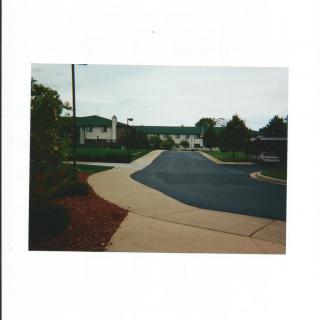A suburban neighborhood street with a sidewalk lined by trees and residential homes.
