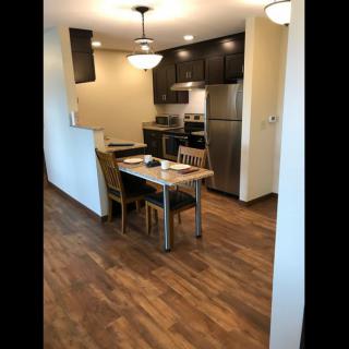 A modern kitchen with stainless steel appliances and a small dining area featuring wood flooring and overhead lighting.