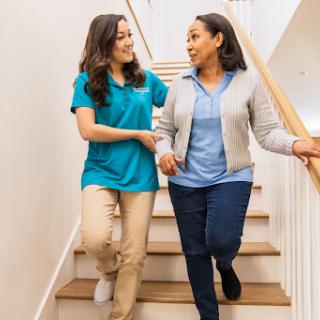 A caregiver assists a person down the stairs, showcasing support and companionship in a healthcare setting.