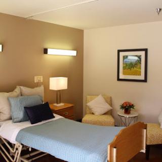A well-lit hospital room featuring a twin bed, cozy seating, and decorative art.