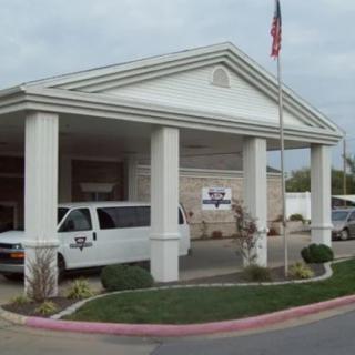 A building entrance with white columns, parked vans, and a flagpole in the foreground.