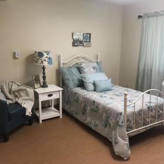 A cozy bedroom with a neatly made bed, nightstand, and comfortable chair.