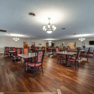 A spacious dining room with wooden floors, featuring tables and chairs under elegant chandeliers.