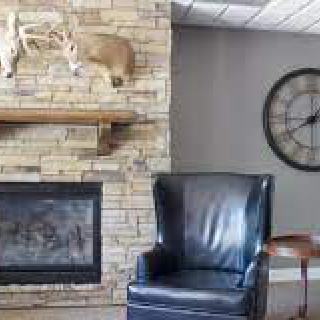 A cozy living room corner with a stone fireplace, leather armchair, and wall-mounted clock.
