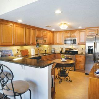 A modern kitchen featuring wooden cabinets, stainless steel appliances, and a granite countertop with bar stools.
