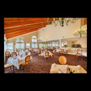 An elegant and spacious restaurant dining room with empty tables, featuring chandeliers and large windows.