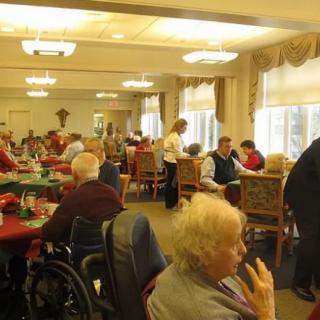 Elderly individuals gather in a dining room for a social event at a nursing home.