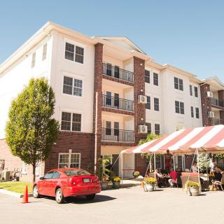 An apartment building with a red car parked in front and a striped tent set up outdoors.