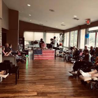 A gathering of people in a spacious indoor area with an American flag displayed prominently.