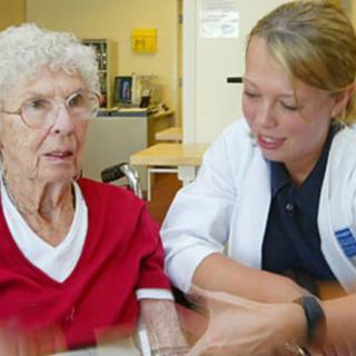 A healthcare worker interacts with an elderly woman in a nursing home setting.