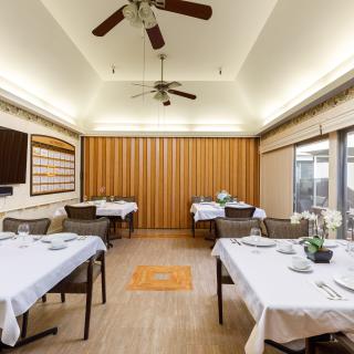 A well-lit dining room with neatly arranged tables covered in white tablecloths.