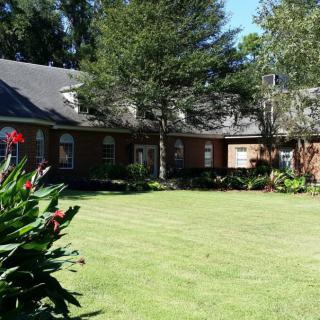 A sunny day view of a brick house surrounded by a well-maintained lawn and garden.