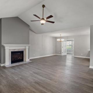 A spacious living room with a fireplace and ceiling fan, featuring hardwood floors and neutral color tones.