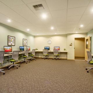 A modern computer room with desks and computers arranged along a wall, featuring fluorescent lighting.