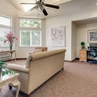 A cozy living room with a couch, large windows, and a ceiling fan.