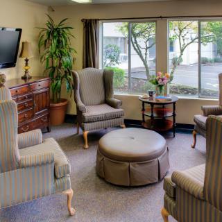A cozy living room with elegant chairs, an ottoman, television, and a large window allowing natural light in.