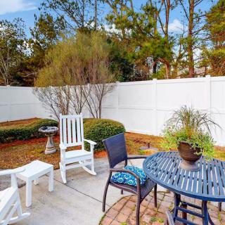 A cozy patio with outdoor furniture including chairs and a table adorned with plants, surrounded by a garden and white fence.