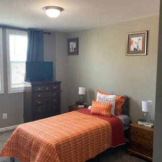 A cozy bedroom with a single bed featuring orange bedding, a dresser with a TV on top, and nightstands with lamps.