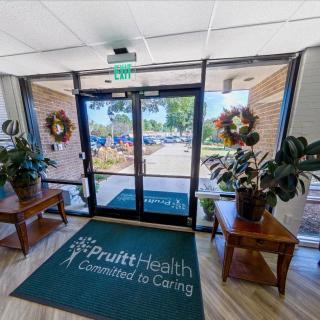 The entrance of PruittHealth, featuring a welcoming mat and decorative plants beside glass doors.