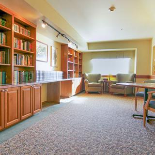 A cozy library space with bookshelves, comfortable seating, and natural light from windows.