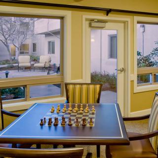 Chess set ready for a game in a cozy, sunlit room overlooking a courtyard.
