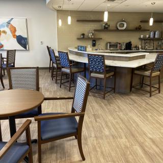 A modern cafe interior featuring a seating area with wooden tables and blue cushioned chairs, alongside a bar counter.