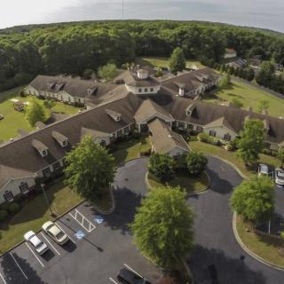 Aerial view of a sprawling building complex surrounded by lush greenery and a parking lot.