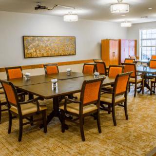 A well-lit dining room with multiple tables and orange-cushioned chairs arranged neatly.