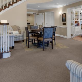 A spacious interior with a dining area featuring a table and chairs, carpeted flooring, and staircase.