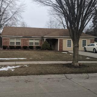 A cozy suburban house during winter, featuring a neatly trimmed lawn and a bare tree.
