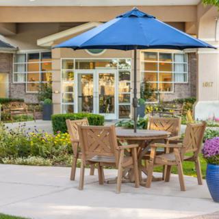 An inviting outdoor patio area with wooden furniture and a blue umbrella, set in front of a building.