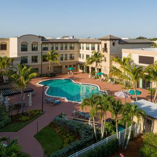 Aerial view of a resort courtyard with a central swimming pool surrounded by buildings and palm trees.