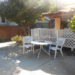 A sunny patio with a table and two chairs surrounded by greenery.