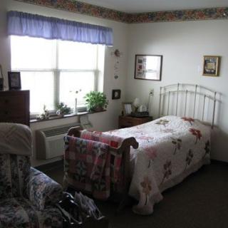 A cozy bedroom with a single bed, decorated with floral patterns and natural light from the window.