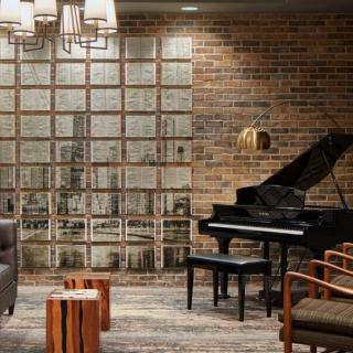 A modern lounge area featuring a grand piano, brick walls, comfortable seating, and stylish lighting.