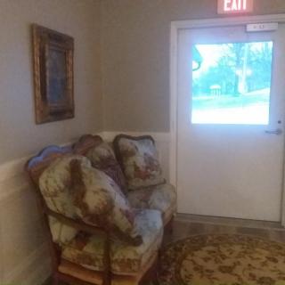 A cozy chair and painting by an exit door in a hallway.
