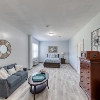 A cozy bedroom with a bed, sofa, coffee table, and dresser, decorated in soft tones.