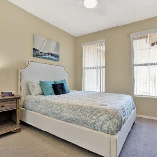 A cozy bedroom with a neatly made bed, two large windows, and wall artwork.