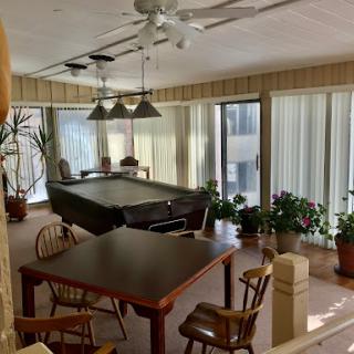 A spacious indoor area featuring a billiards table and a dining table surrounded by large windows and potted plants.