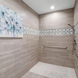 A modern shower with beige tiles and a decorative tile band, featuring a grab bar and wall artwork.