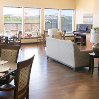 A bright living and dining area with wooden floors, featuring a piano and large windows.