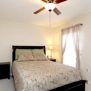 A cozy bedroom with a neatly made bed, ceiling fan, and soft lighting.