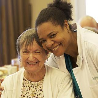 A nurse smiling alongside an elderly woman, showcasing companionship and care in a healthcare setting.