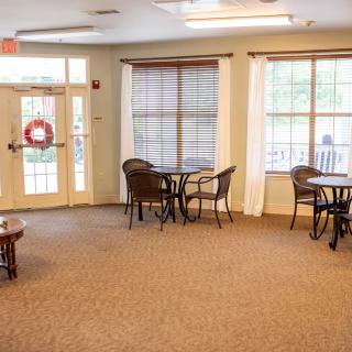 A brightly lit lobby area with tables and chairs, featuring large windows and carpeted flooring.