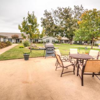An inviting outdoor patio with a table, chairs, and grill set against a backdrop of a well-maintained lawn and trees.