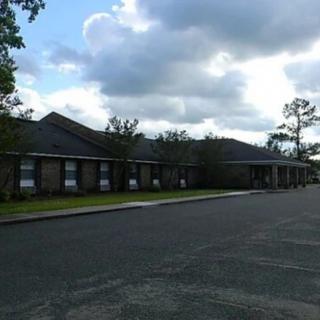 A long brick building under a cloudy sky with a sidewalk and an asphalt road in the foreground.