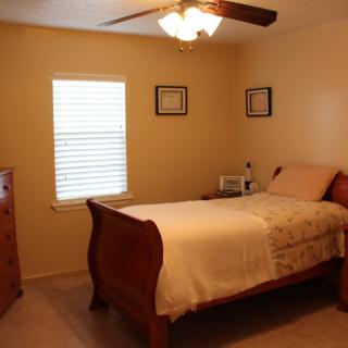 A cozy bedroom with a single bed, dresser, and ceiling fan.
