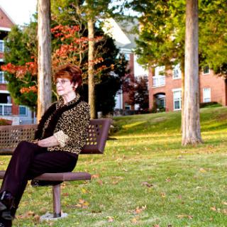 A woman sitting on a bench in a park surrounded by trees and the vibrant colors of autumn.