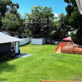 A green backyard featuring a wooden deck, two sheds, and surrounded by trees.